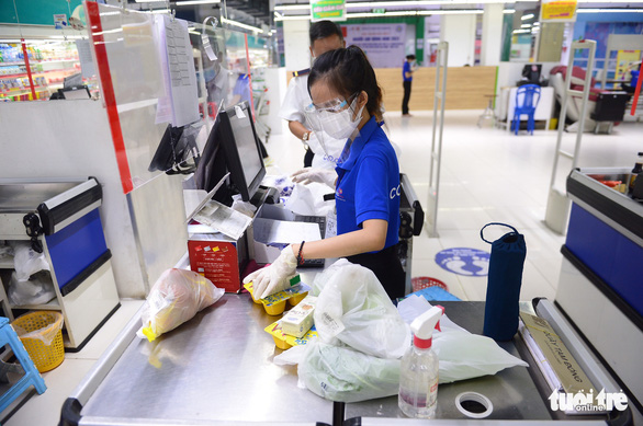 A cashier in a Co.opmart supermarket in Ho Chi Minh City wears a face protection shield while checking out items for customers. Photo: Quang Dinh / Tuoi Tre