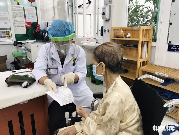 A doctor at the Ho Chi Minh City Traditional Medicine Institute gives Nguyen Thi Ton, 102, her certificate of vaccination against COVID-19, August 8, 2021. Photo: Dinh Tuan / Tuoi Tre