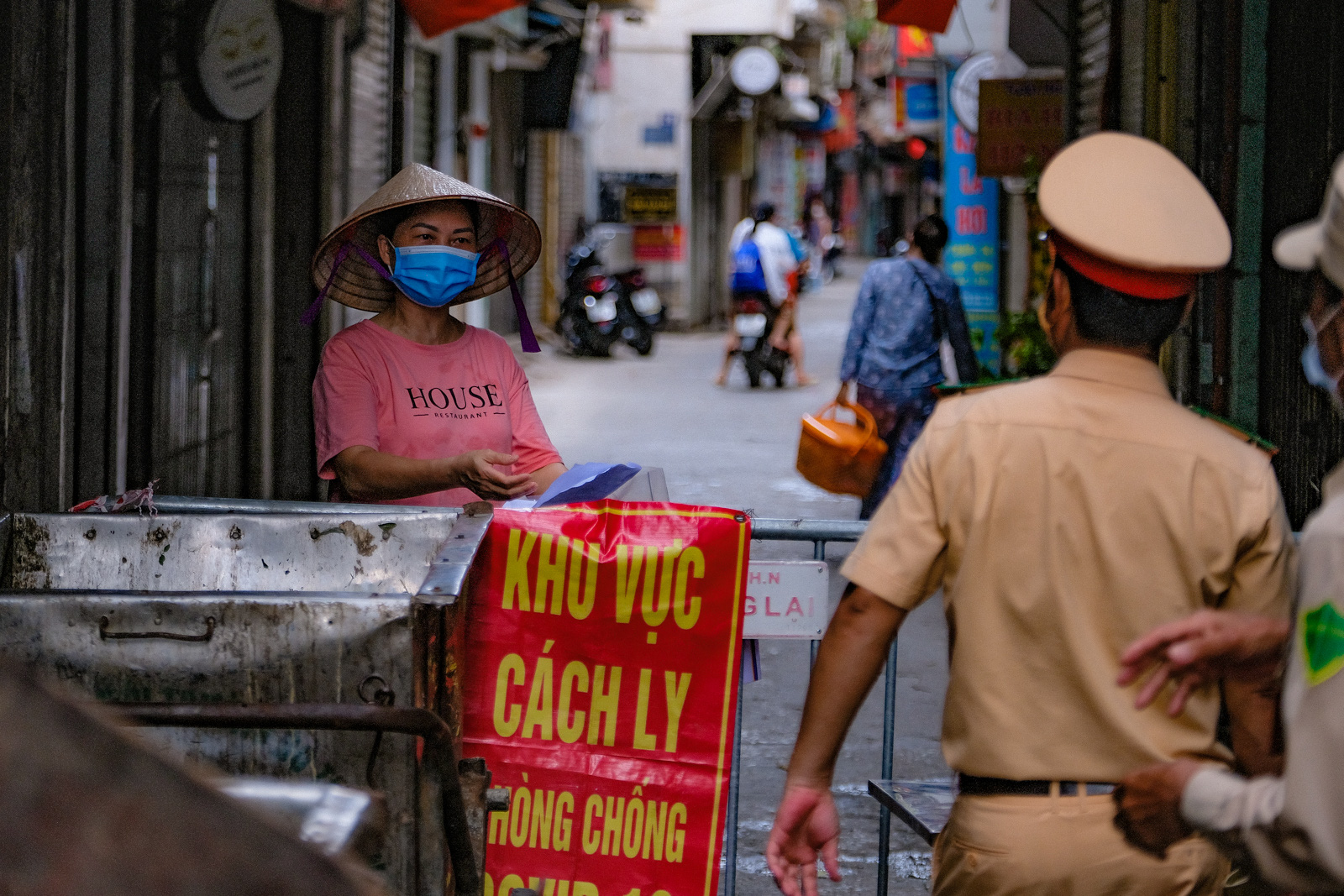 People receive food through a barricade set up at an entrance to a locked-down residential area in Dong Da District, Hanoi, August 5, 2021. Photo: Nam Tran / Tuoi Tre