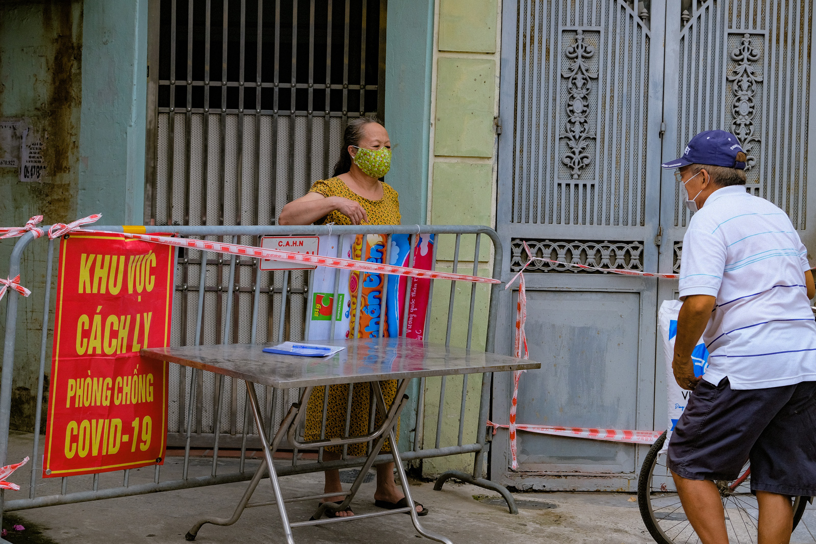 People receive food through a barricade set up at an entrance to a locked-down residential area in Dong Da District, Hanoi, August 5, 2021. Photo: Nam Tran / Tuoi Tre