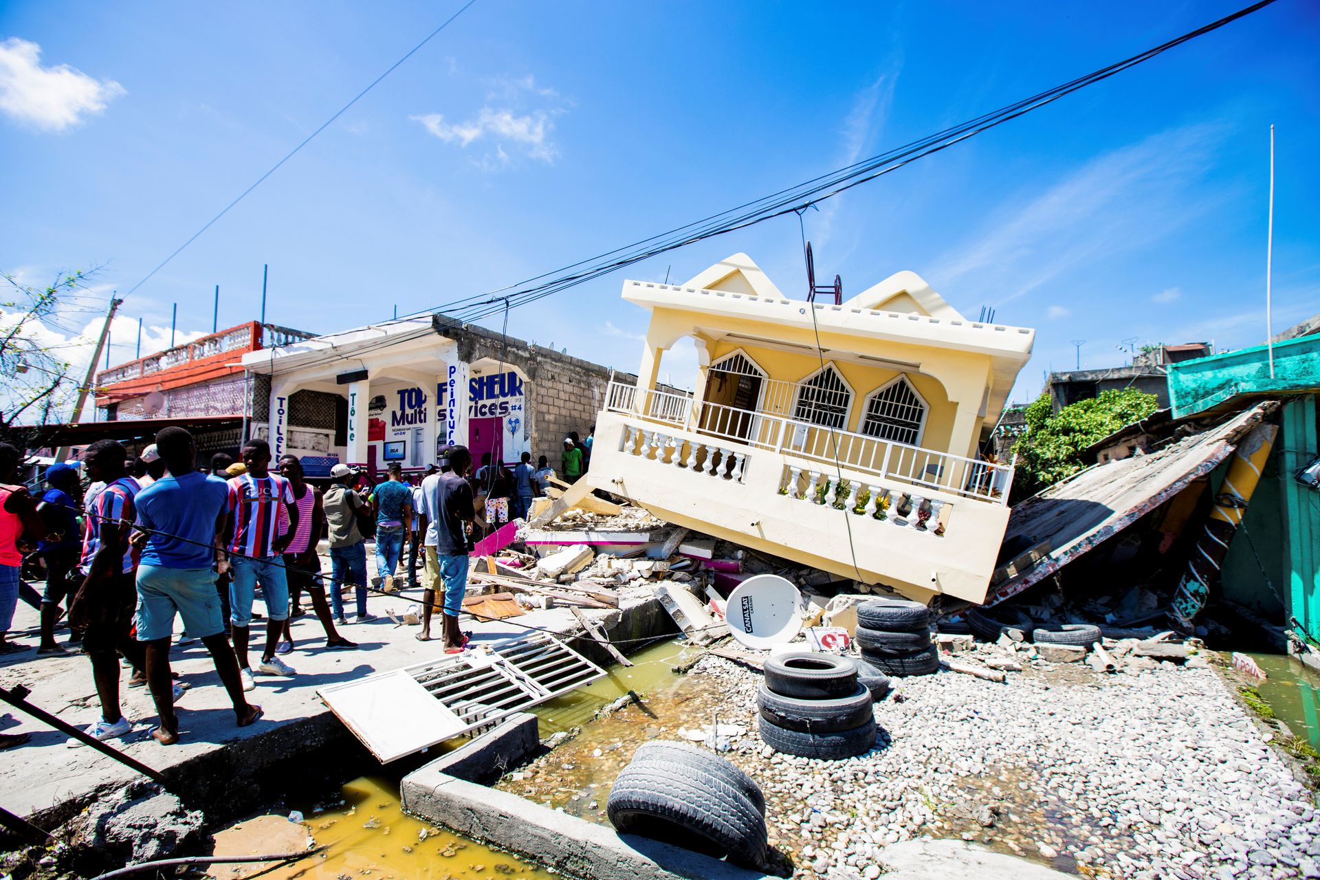 People stand next to a house destroyed following a 7.2 magnitude earthquake in Les Cayes, Haiti August 14, 2021. Photo: Reuters