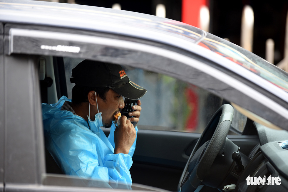 Huynh Quang Nhat Long eats a piece of cake in the car while taking a phone call on a trip delivering oxygen cylinders. Photo: Duyen Phan / Tuoi Tre News