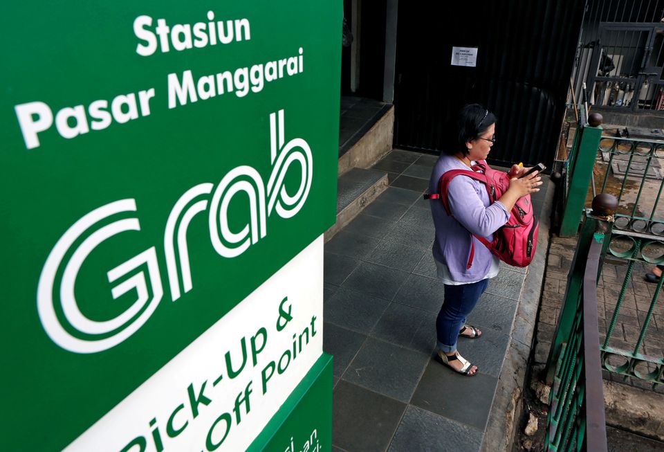 A woman uses her phone near a sign for the online ride-hailing service Grab at the Manggarai train station in Jakarta, Indonesia July 3, 2017. Photo: Reuters