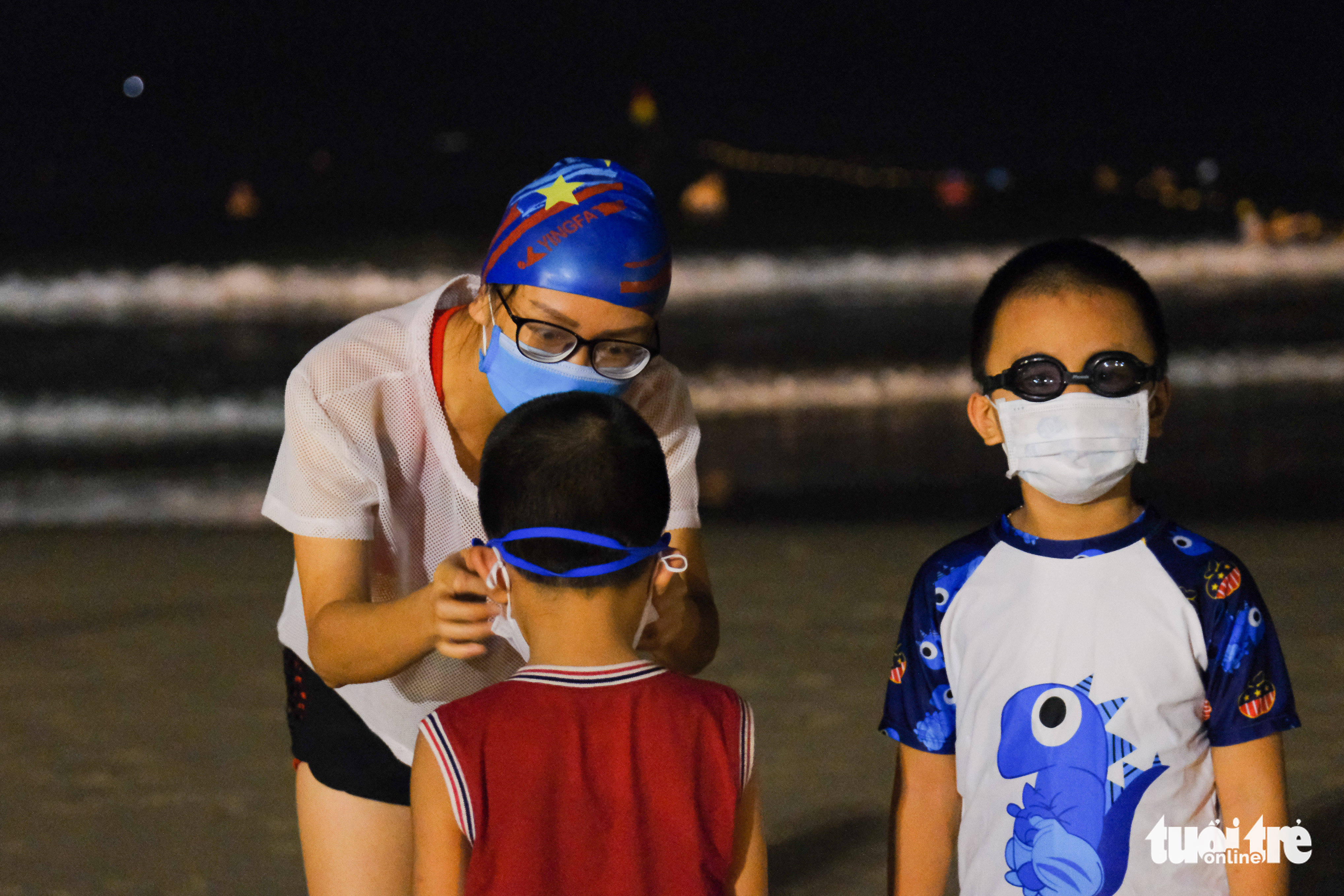 A woman helps her son put on a face mask and swimming goggles at a beach in Da Nang, September 30, 2021. Photo: Tan Luc / Tuoi Tre