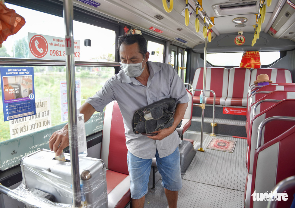 A bus goer in Ho Chi Minh City puts ticket money in a box, October 5, 2021. Photo: Ngoc Phuong / Tuoi Tre