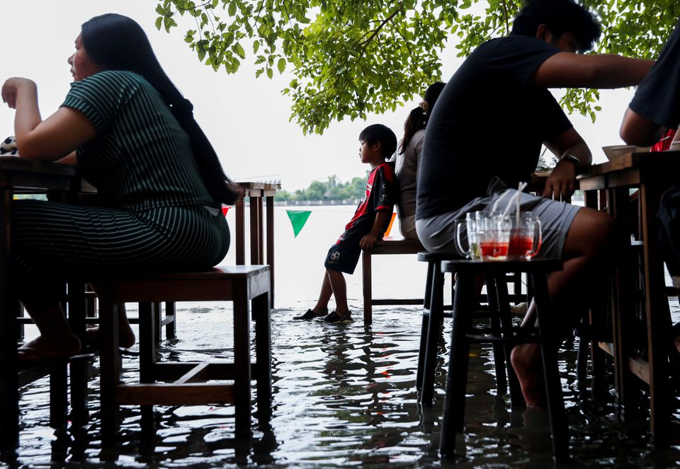 People eat food at a flooded restaurant, where patrons stand up from their tables every time the waves come in, on a river bank in Nonthaburi near Bangkok, Thailand, October 7, 2021. Photo: Reuters