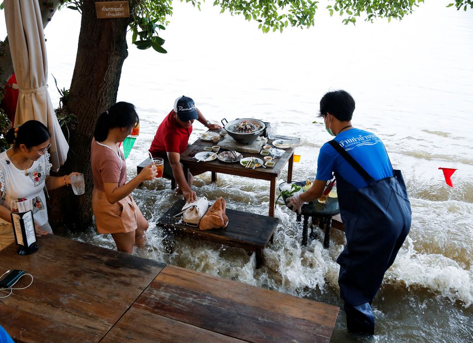 People eat food at a flooded restaurant, where patrons stand up from their tables every time the waves come in, on a river bank in Nonthaburi near Bangkok, Thailand, October 7, 2021. Photo: Reuters