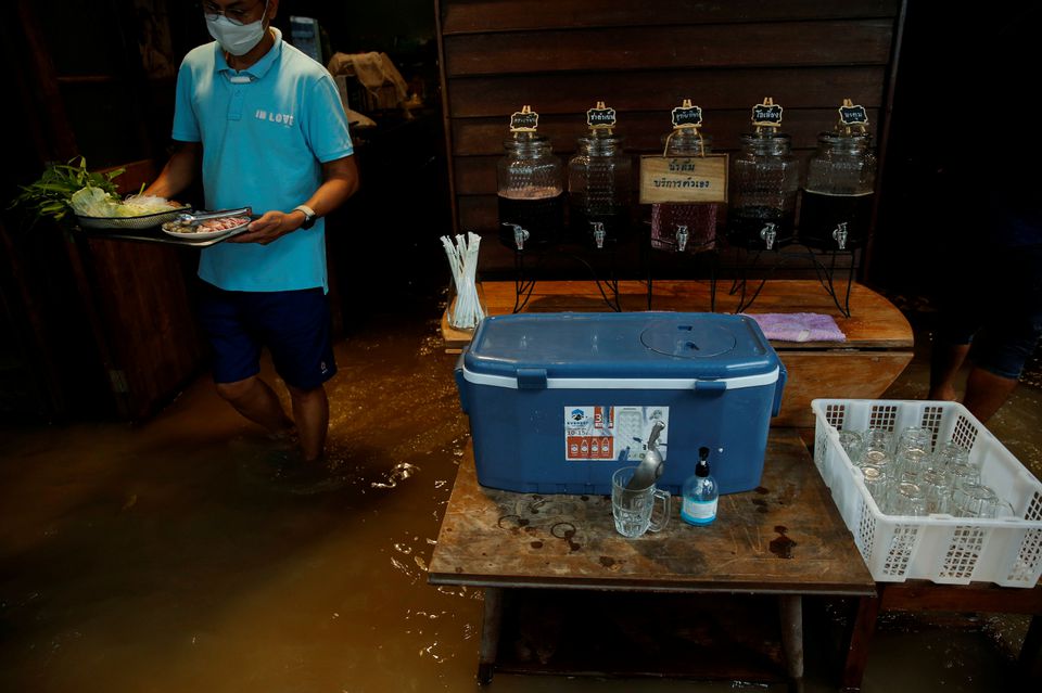 A staff member prepares food for customers at a flooded restaurant, where patrons stand up from their tables every time the waves come in, on a river bank in Nonthaburi near Bangkok, Thailand, October 7, 2021. Photo: Reuters