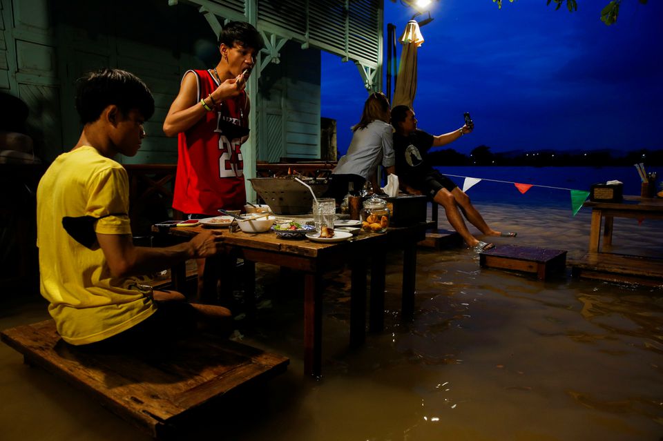 People eat food at a flooded restaurant, where patrons stand up from their tables every time the waves come in, on a river bank in Nonthaburi near Bangkok, Thailand, October 7, 2021. Photo: Reuters