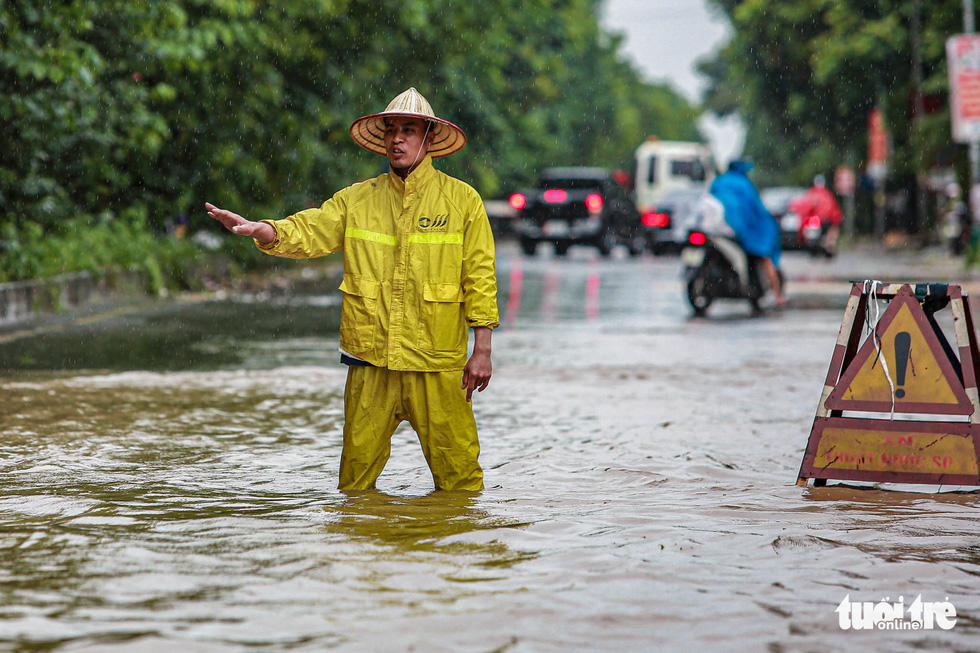 A staffer of the Hanoi Drainage and Sewage Company guides traffic through the flood, October 11, 2021. Photo: Nam Tran / Tuoi Tre