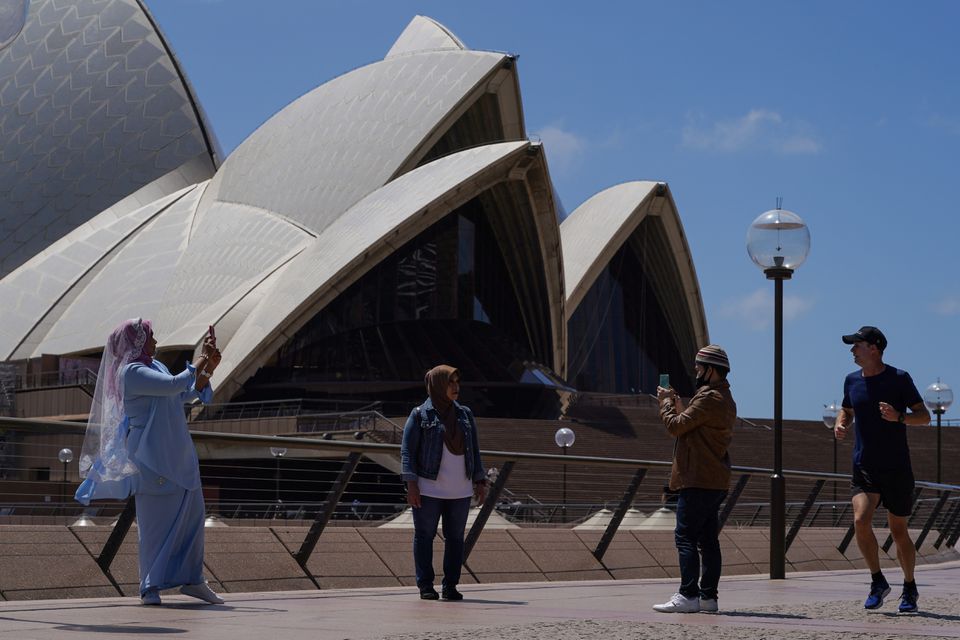 A jogger runs past people taking pictures in front of the Sydney Opera House in the wake of coronavirus disease (COVID-19) regulations easing, following months of lockdown orders to curb an outbreak, in Sydney, Australia, October 19, 2021. Photo: Reuters
