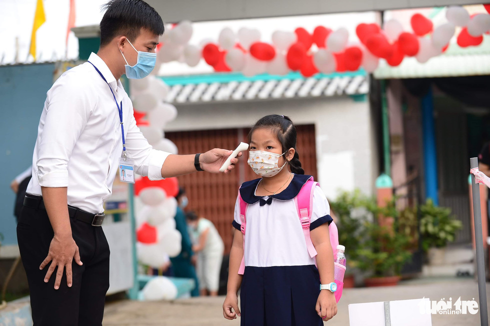 A staff member measures the body temperature of a student in Thanh An Commune, Can Gio District, Ho Chi Minh City, October 20, 2021. Photo: Quang Dinh / Tuoi Tre