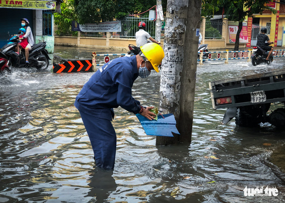 A staffer from the Ho Chi Minh City Urban Drainage Company clears debris from a sewer to drain floodwaters from a street in Ho Chi Minh City, October 21, 2021. Photo: Chau Tuan / Tuoi Tre