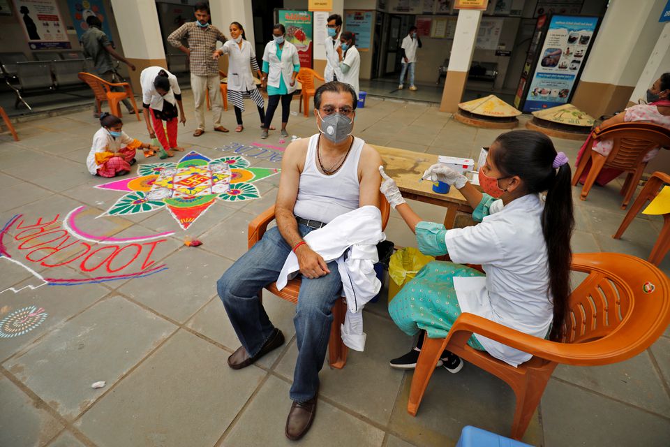 A healthcare worker gives a dose of the COVISHIELD vaccine against the coronavirus disease (COVID-19), manufactured by Serum Institute of India, to a man as others decorate the vaccination centre to celebrate the milestone of administering one billion COVID-19 vaccine doses, in Ahmedabad, India, October 21, 2021. Photo: Reuters