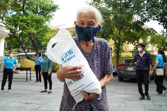 An elderly woman carries a pack of rice received in exchange for cardboard. Photo: Le Trung / Tuoi Tre