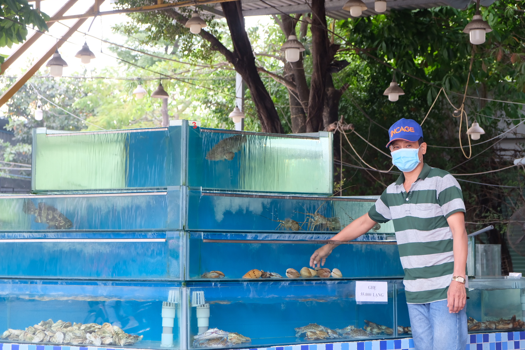 Sang, staffer at a food stall in Thu Duc City, Ho Chi Minh City, is seen near a seafood tank operating at low capacity, November 2021. Photo: Bong Mai / Tuoi Tre