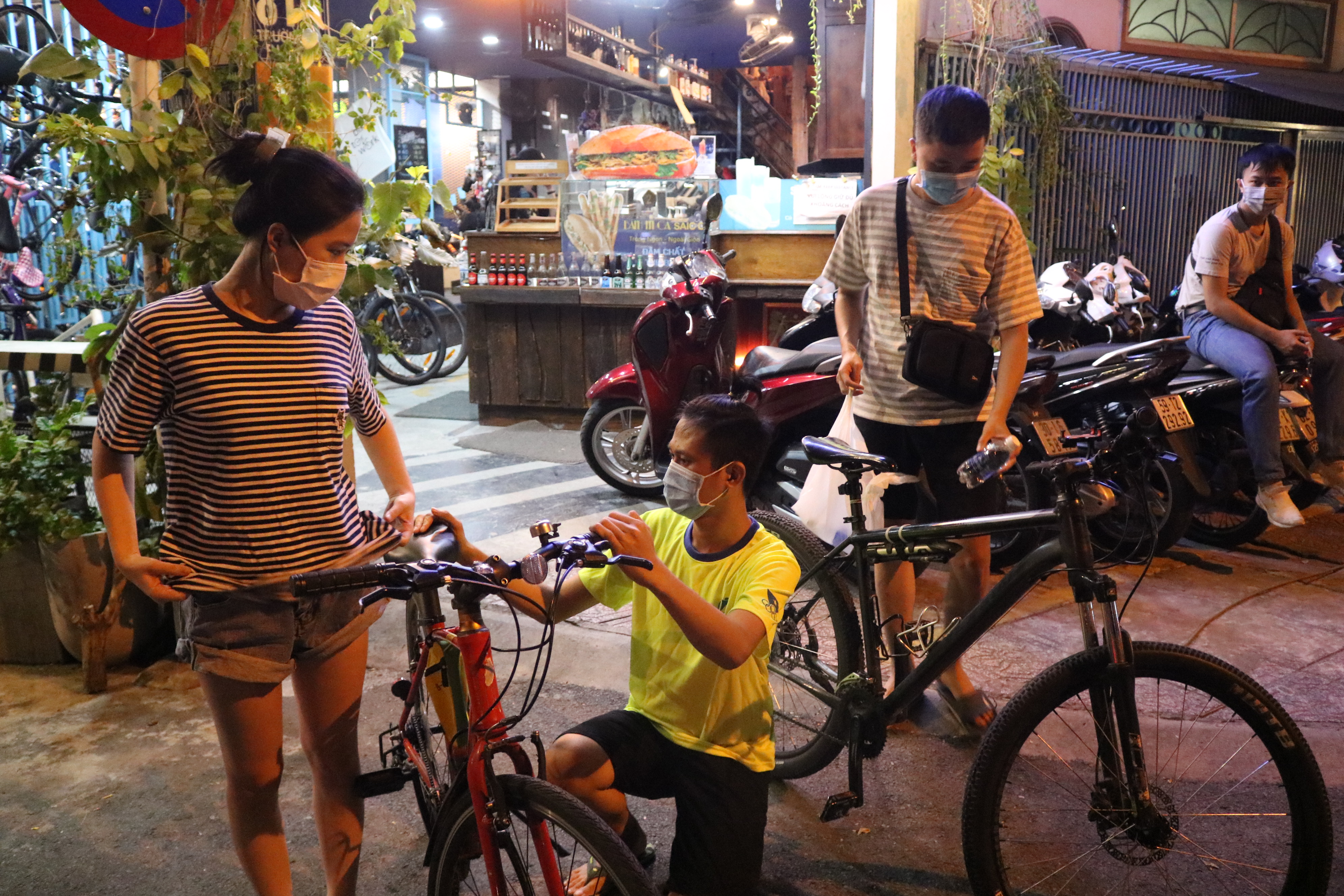 Min (center), a staff member at The Bike Coffee, adjusts a bike seat for a customer at The Bike Coffee in District 3 in Ho Chi Minh City on November 3, 20201. Photo: Hoang An / Tuoi Tre News