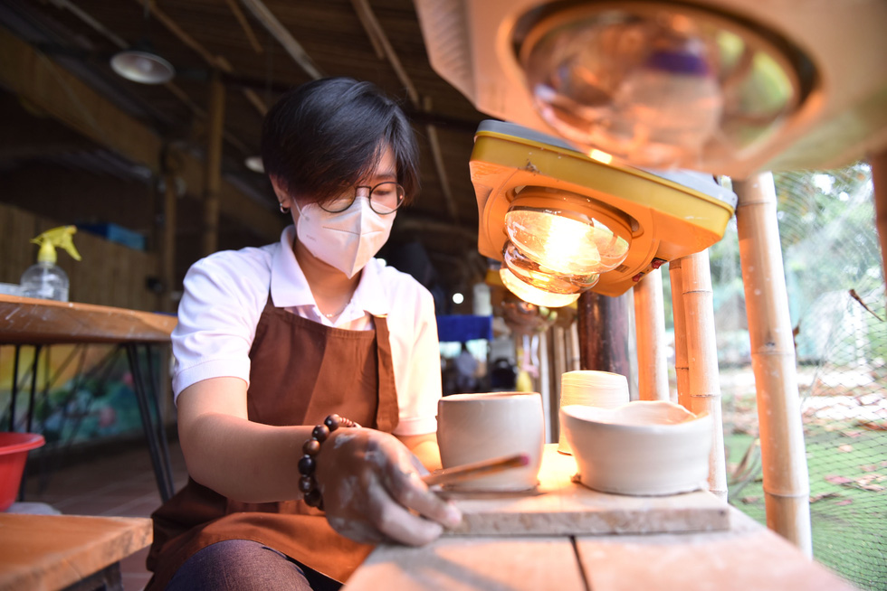 An instructor dries formed pottery under a light for 15 to 30 minutes. Photo: Ngoc Phuong – Hoang An / Tuoi Tre.