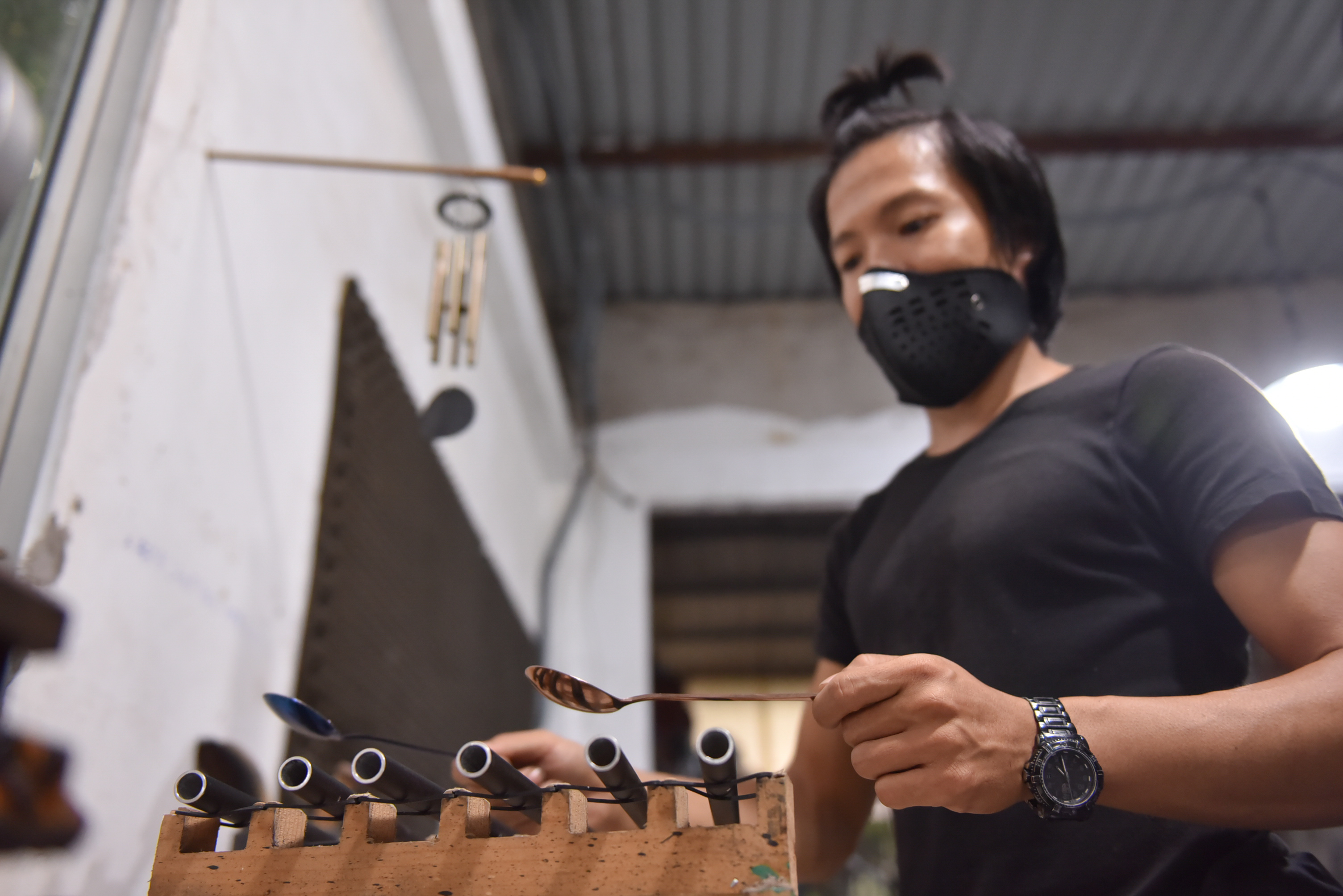 Tran Ngoc Hong Duc uses two spoons to test the sound of a number of tubes prepared to be assembled into wind chimes. Photo: Ngoc Phuong / Tuoi Tre News