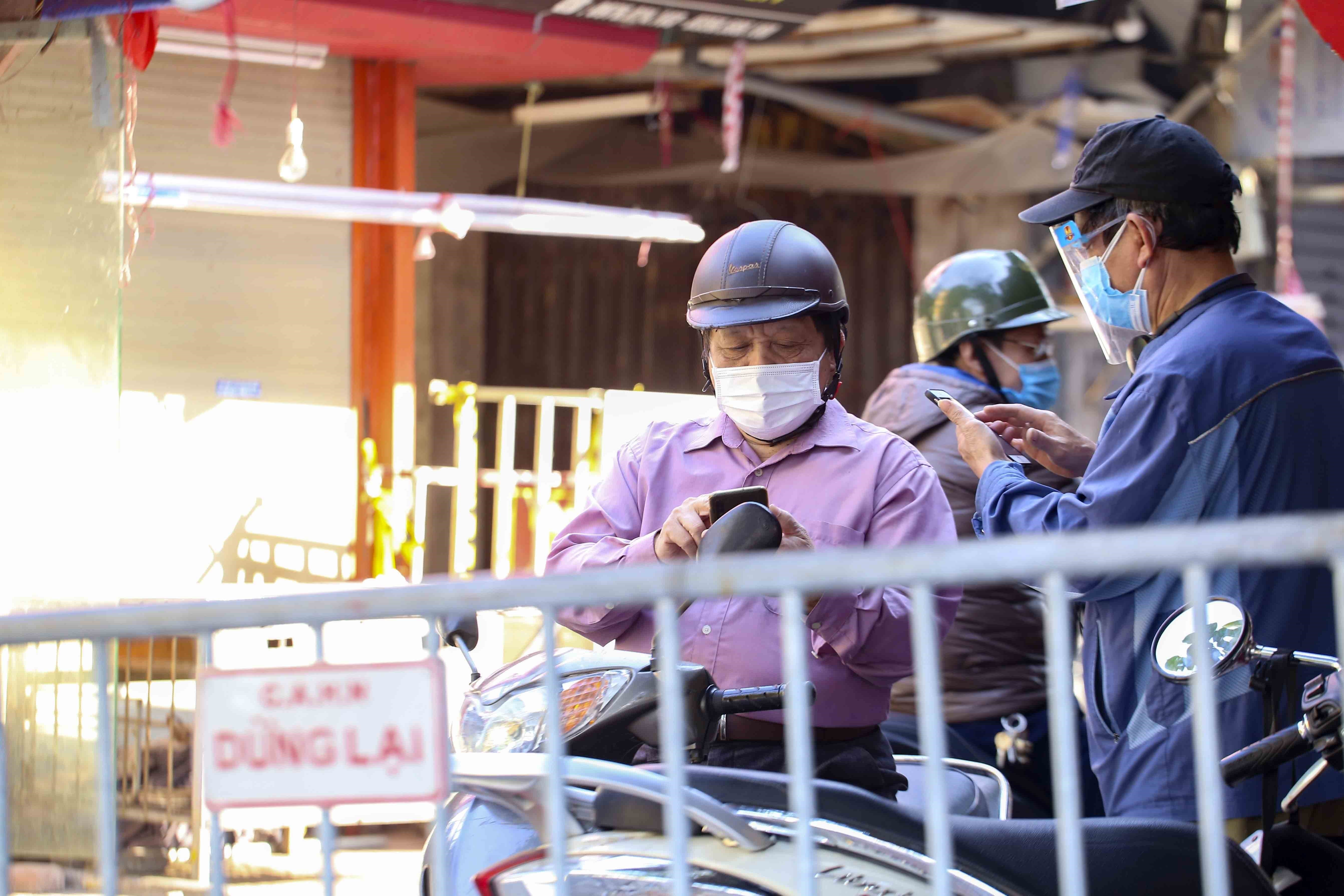 A functional force member checks a commuter for a health declaration on a smartphone at a COVID-19 checkpoint near Nguyen Cong Tru Market in Pho Hue Ward, Hai Ba Trung District, Hanoi, December 5, 2021. Photo: Vietnam News Agency