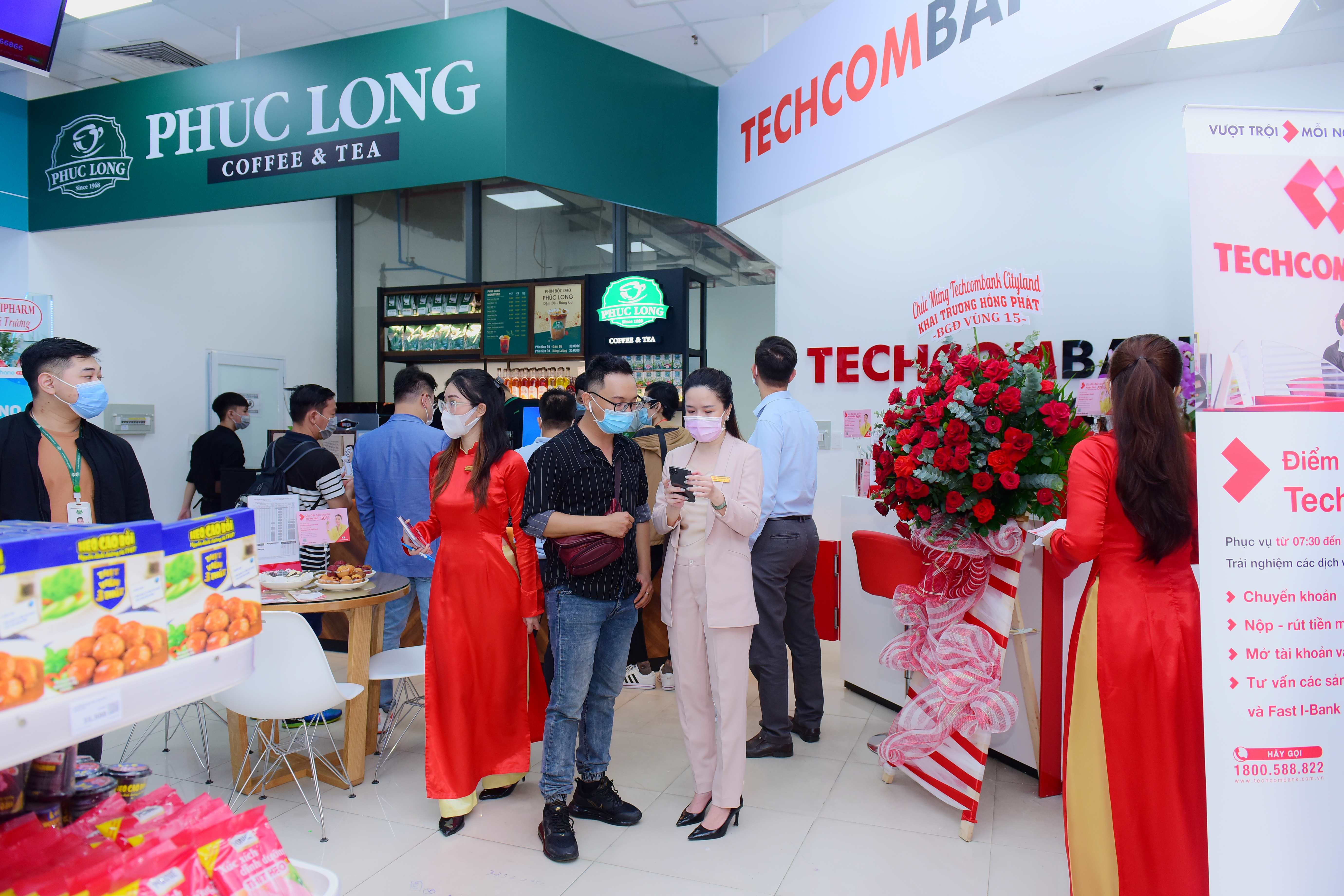 A Phuc Long coffee - tea kiosk is set up next to a Techcombank transaction counter inside a WinMart+ store.