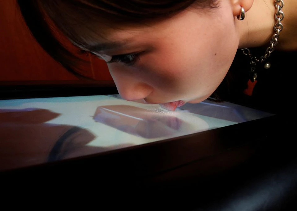 A demonstrator licks the screen of Taste the TV (TTTV), a prototype lickable TV screen that can imitate the flavours of various foods, during its demonstration at the university in Tokyo, Japan, December 22, 2021. Picture taken December 22, 2021. Photo: Reuters
