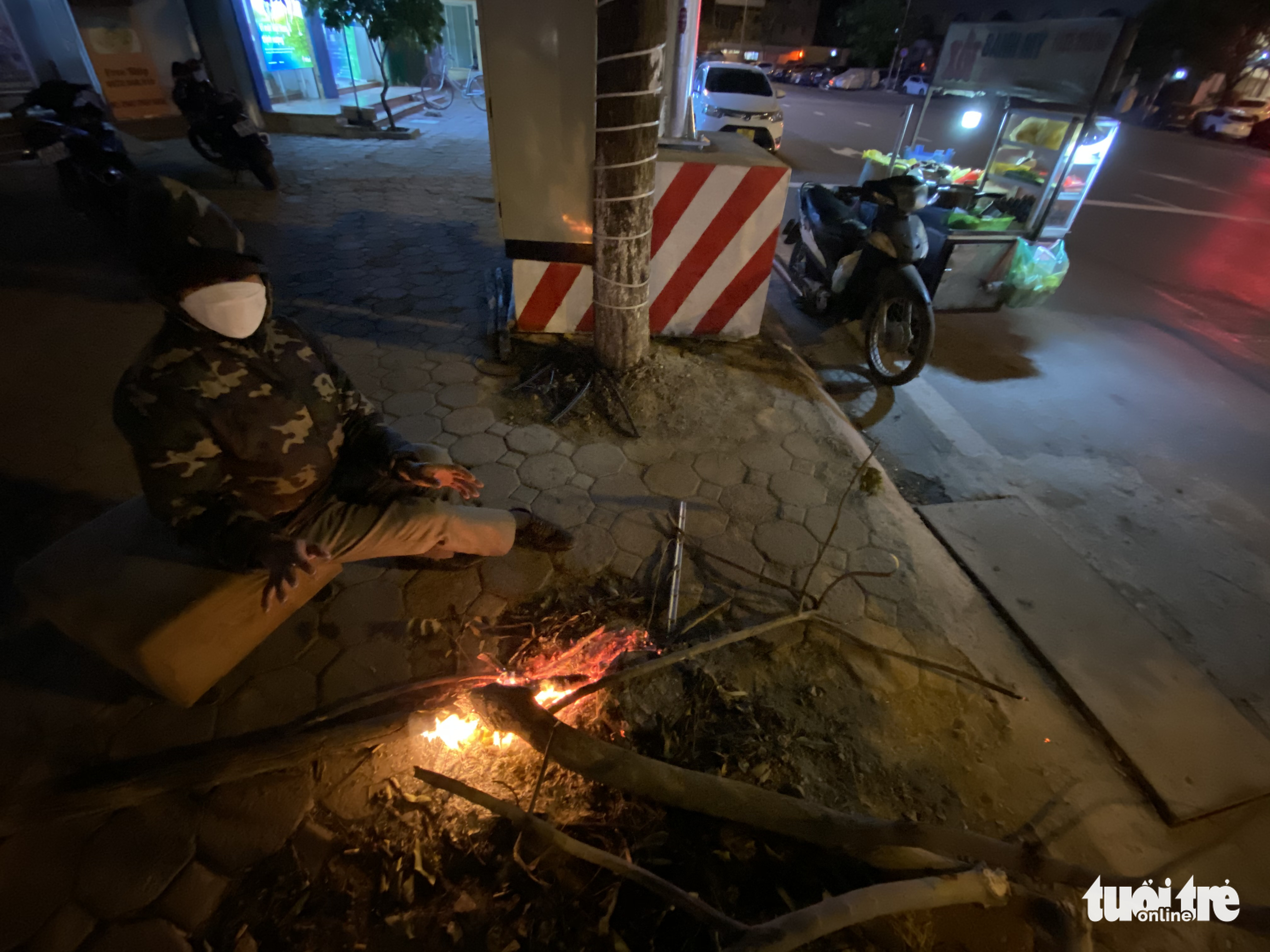 A street food vendor sits by a bonfire on a sidewalk in Hanoi, December 27, 2021. Photo: Tuoi Tre