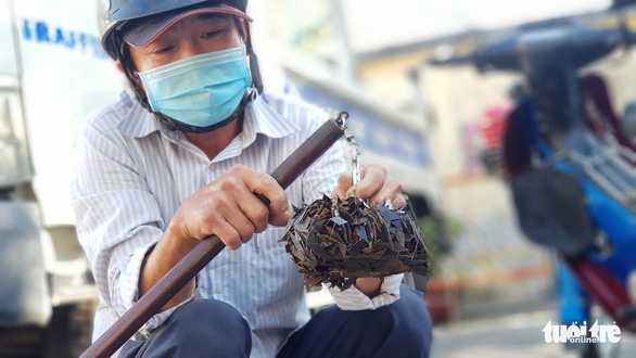 Dinh Minh Canh holds a stick of magnet sticking a lot of sharp metal tire-puncturing nails. Photo: Ngoc Khai / Tuoi Tre