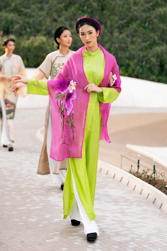 A delicate Vietnamese traditional costume by Vu Viet Ha with a pink floral embroidered shawl symbolising Vietnam’s natural wonder, stands out in her sheen green Ao Dai.