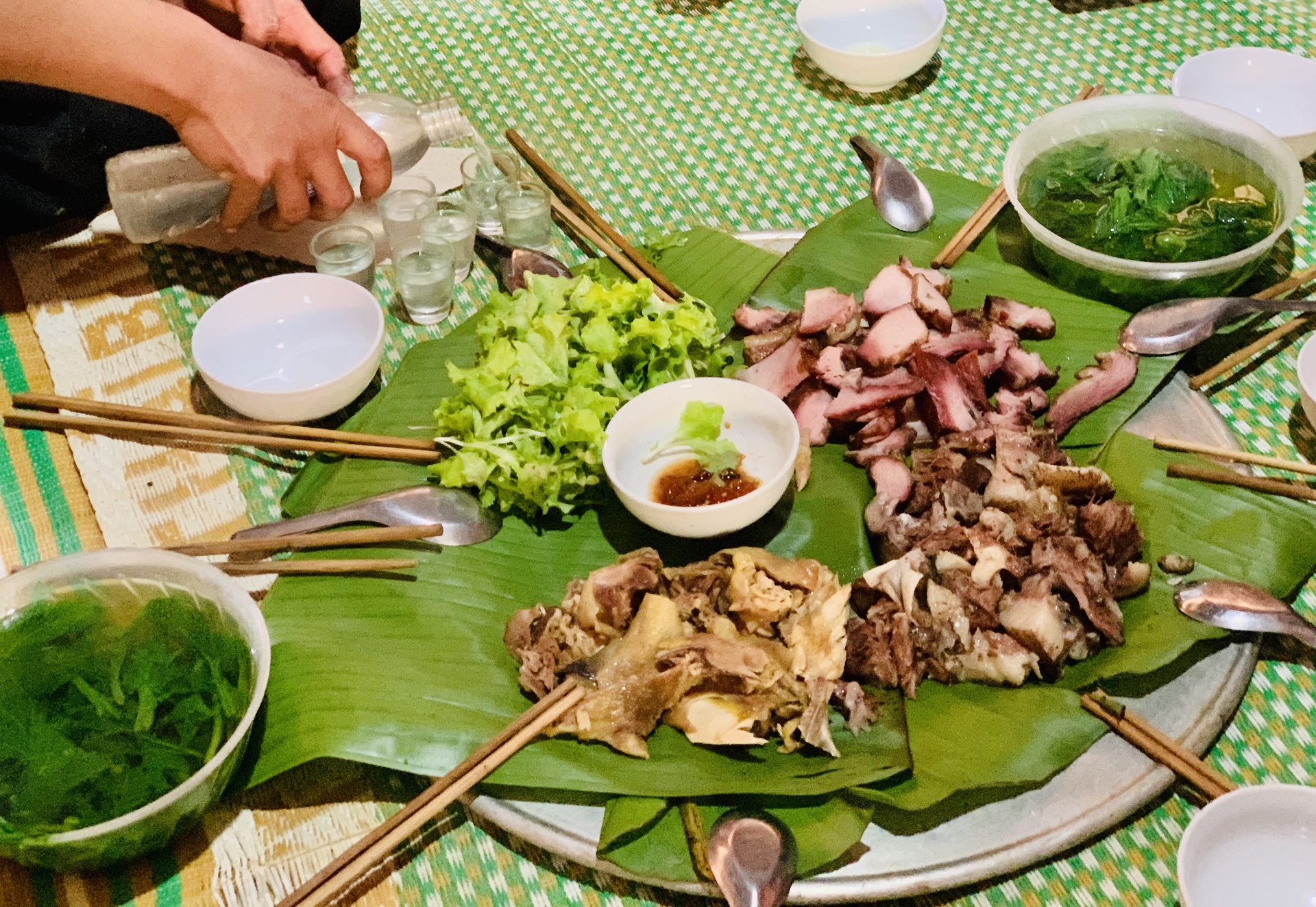 The family serving plate of the Mong has banana leaves on which meat is grouped by type. This serving plate is on the floor and diners sit with their legs crossed, enjoy their foods and tiny glasses of wine.