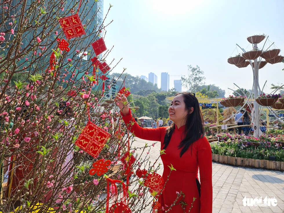 A lady in beautiful red Ao Dai poses for photos next to the blooming apricot peach blossom. Photo: Cong Trieu / Tuoi Tre