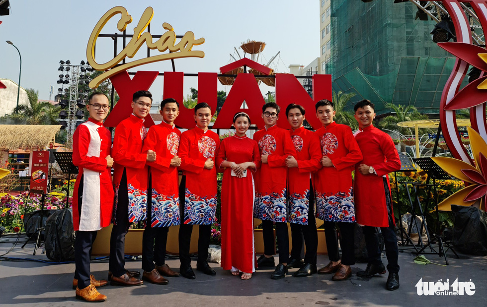 Young lady and men in red Ao Dai stand in front of the Spring Flower Festival gate. Photo: Cong Trieu / Tuoi Tre