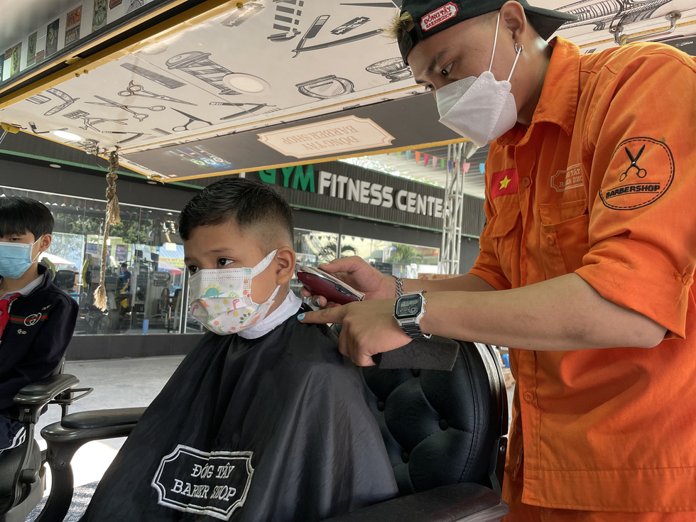 Nguyen Thanh Manh is giving a free haircut to the five-year-old Kim An Nguyen, whose grandfather and father lost their lives to the coronavirus. Photo: Vu Thuy / Tuoi Tre
