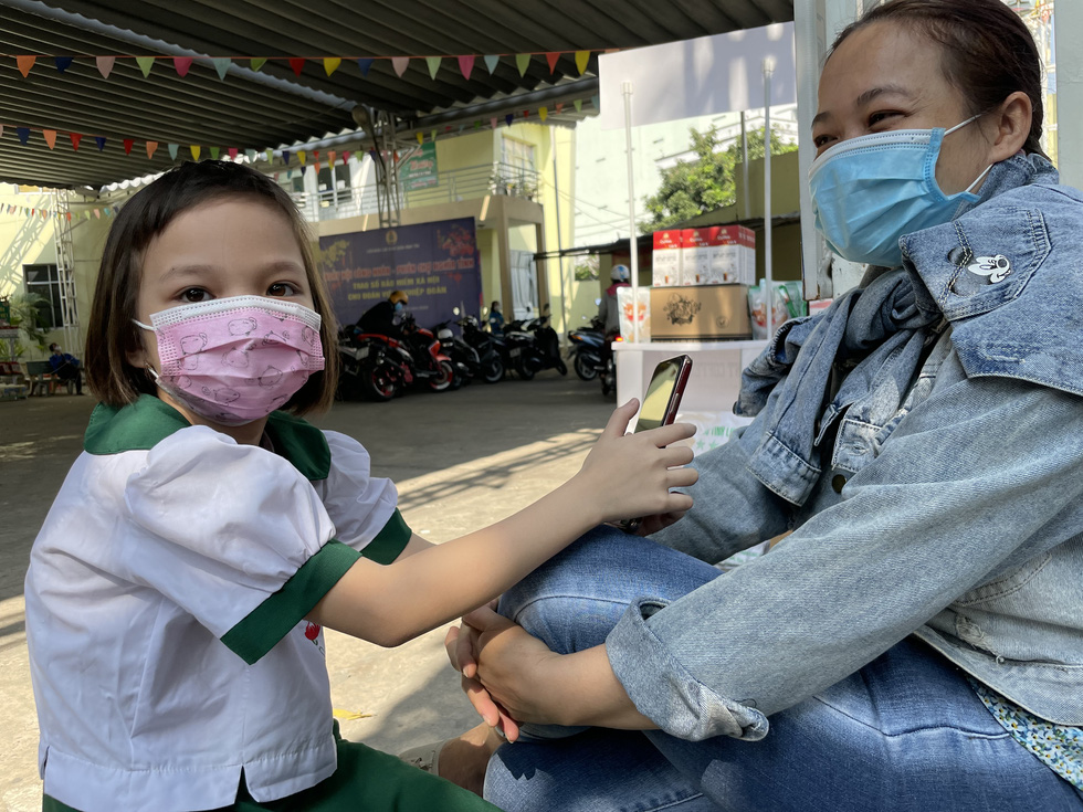 The 9-year-old Vo Le Ngoc Han, who lost her father and grandma during the pandemic, is sitting with her mother to wait for her turn. Photo: Vu Thuy / Tuoi Tre