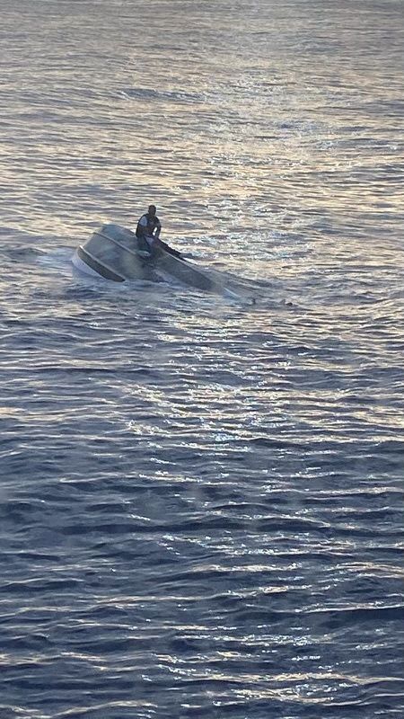 A man, who says he was one of 40 people who left Bimini, Bahamas, on Saturday before encountering severe weather, sits on a capsized boat off the coast of Fort Pierce Inlet, Florida, U.S., in this photo released by the U.S. Coast Guard on January 25, 2022. Courtesy of U.S. Coast Guard/Handout via REUTERS