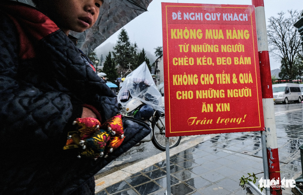 This image shows a child standing by a board that calls on travelers not to buy goods from street vendors or donate money to beggars in Sa Pa Town.