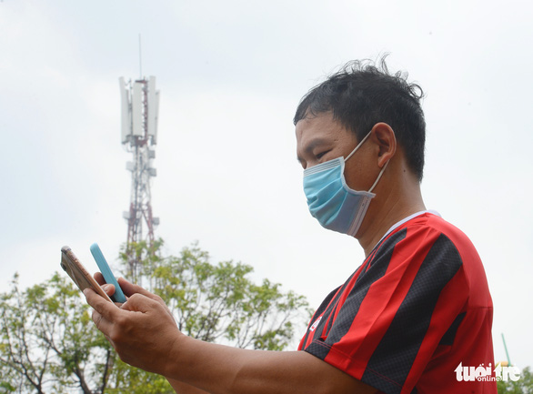 A man holds two mobile devices in his hands, with a distant cell tower in the background. Photo: Tu Trung - Tuoi Tre