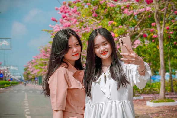 Two women take selfies with the blooming rosy trumpet flower trees in Chau Thanh District, Soc Trang Province, Vietnam. Photo: T.Luy / Tuoi Tre