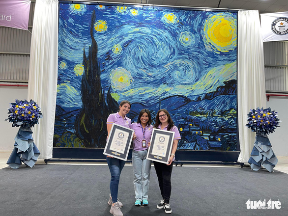 Nguyen Pham Thi Diem Huong (middle) and her staffs pose for a photo with the world-record painting background. Photo: N.H. / Tuoi Tre