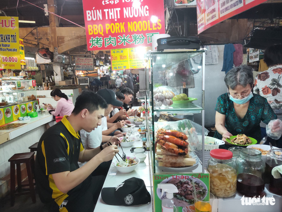 Food stalls at the market become busier. The photo shows a group of Hanoians excitedly trying rice noodle soup at an eatery at Ben Thanh Market. Photo: N.Tri / Tuoi Tre
