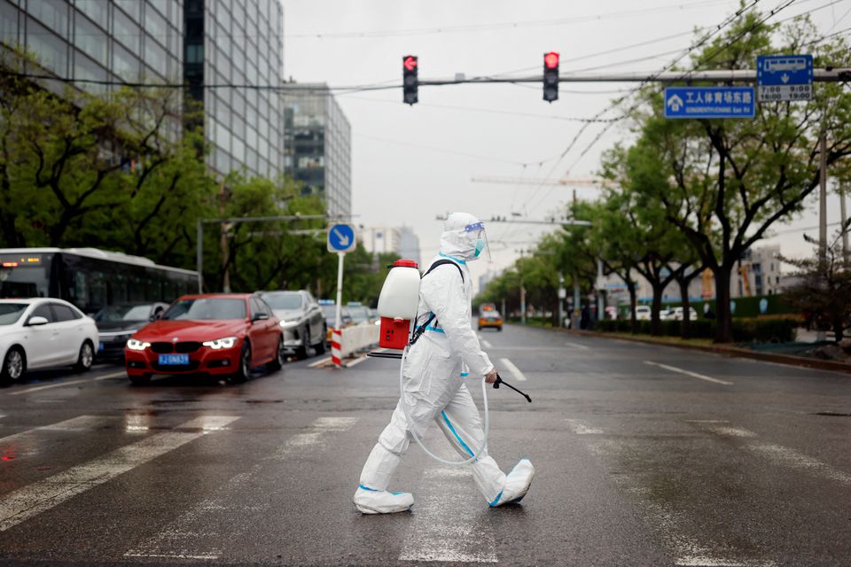 A worker wearing a protective suit and carrying disinfection equipment crosses a road amid the coronavirus disease (COVID-19) outbreak in Beijing, China April 27, 2022. Photo: Reuters