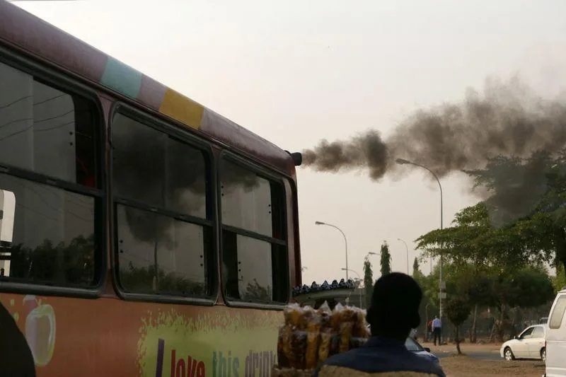 A man sells plantain chips near a bus with smoke seen from its exhaust at a bus park in Abuja. Photo: Reuters