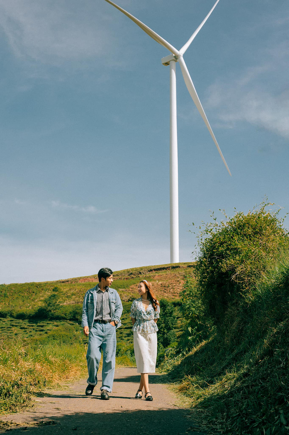 A couple poses for a photo in front of a wind turbine background at Cau Dat Tea Farm in Da Lat City's Xuan Truong Commune. Photo: Nguyen Hien / Tuoi Tre