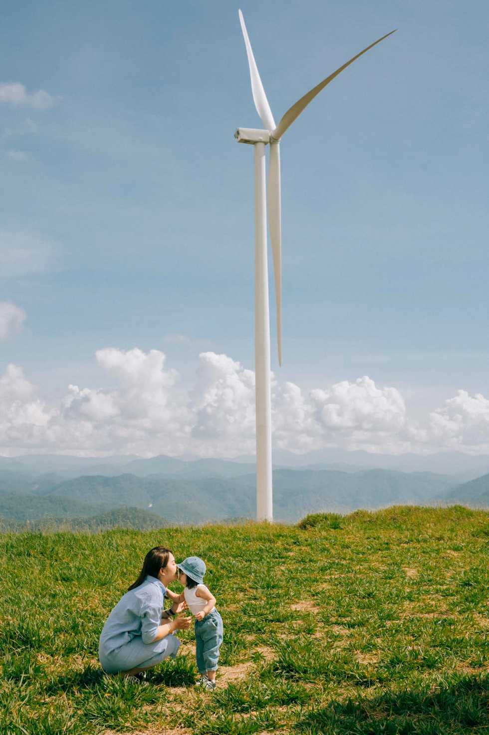 A child and her mom pose for a photo in front of a wind turbine background at Cau Dat Tea Farm in Da Lat City's Xuan Truong Commune. Photo: Nguyen Hien / Tuoi Tre