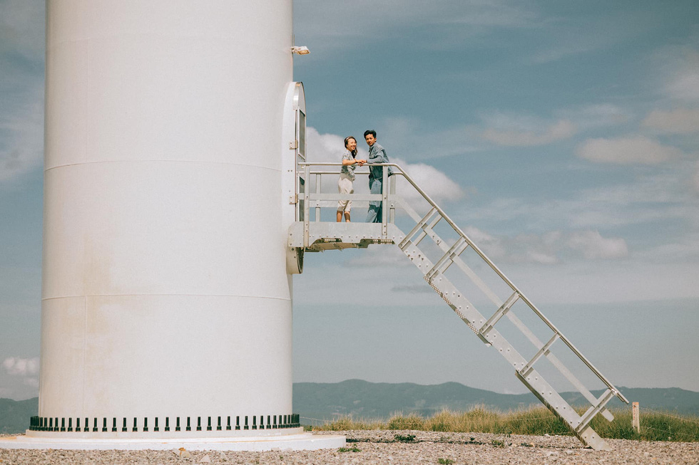 A couple poses for a photo at a wind turbine at Cau Dat Tea Farm in Da Lat City's Xuan Truong Commune. Photo: Nguyen Hien / Tuoi Tre