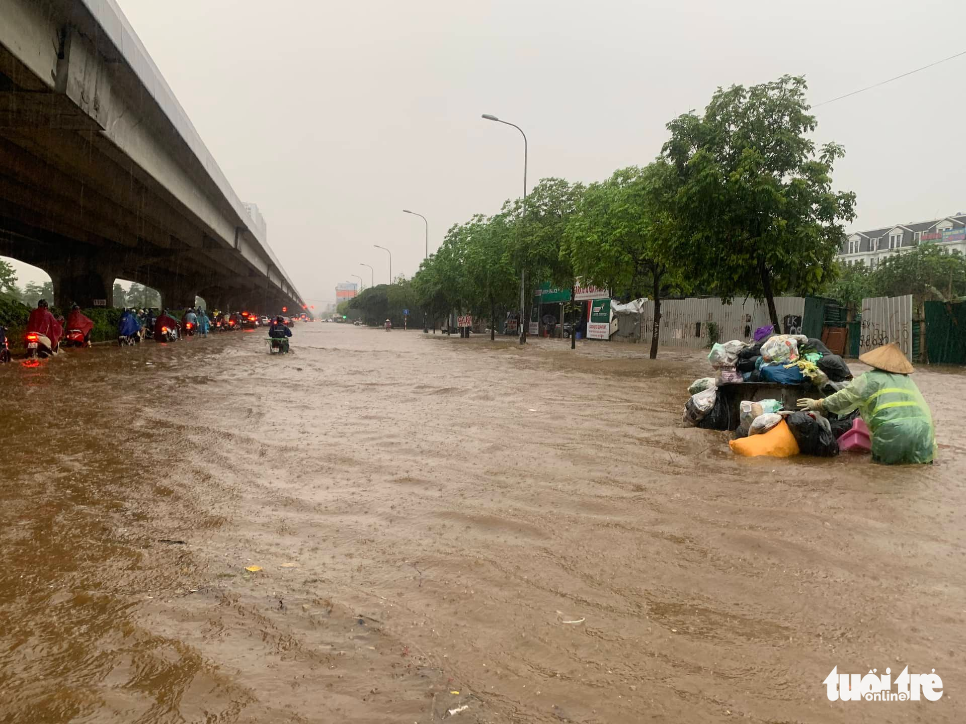 A sanitary worker pushes a garbage trolley through flooded Ring Road 3 in Hanoi, May 29, 2022. Photo: Thanh Chung / Tuoi Tre
