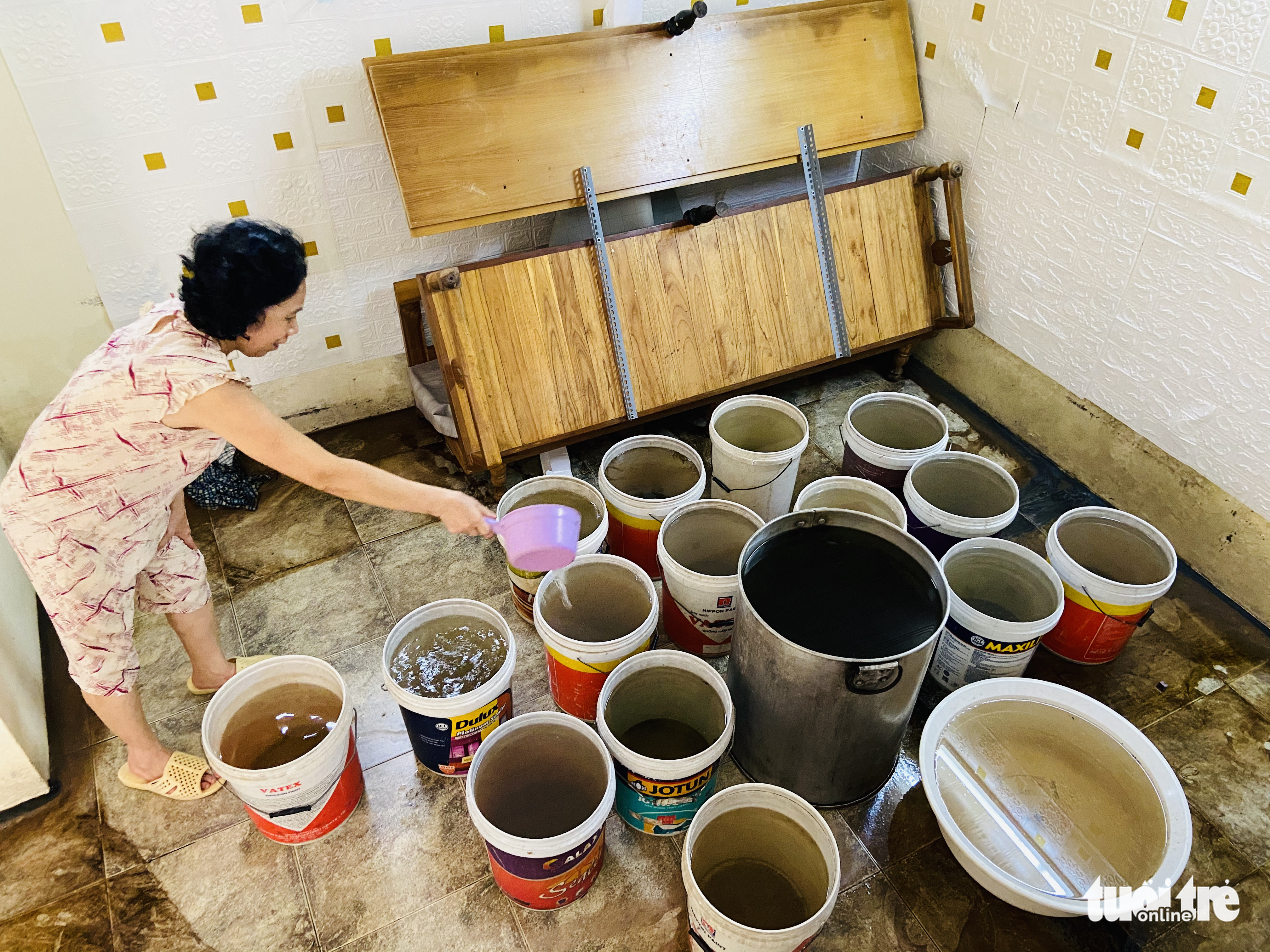 A woman pours floodwater into multiple barrels at her house in Tay Ho District, Hanoi. Photo: Quang The / Tuoi Tre