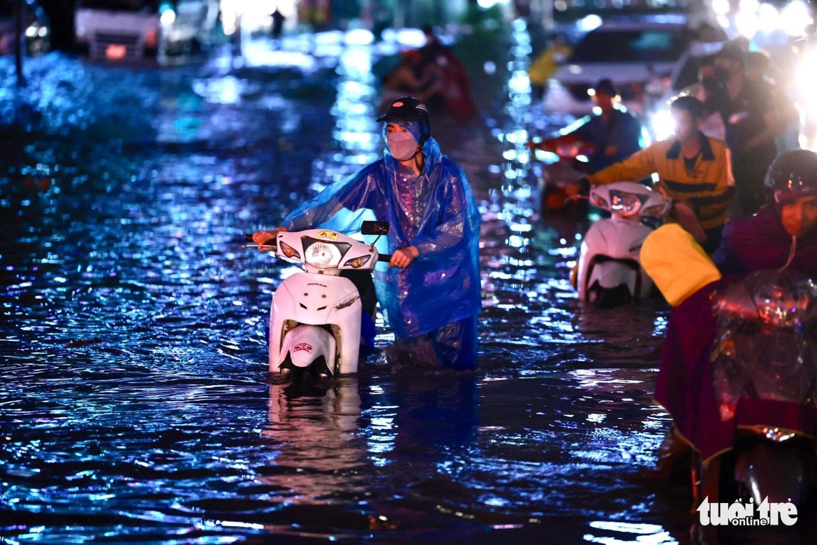 Commuters push their motorbikes along a flooded street in Hanoi, June 13, 2022. Photo: Tuoi Tre