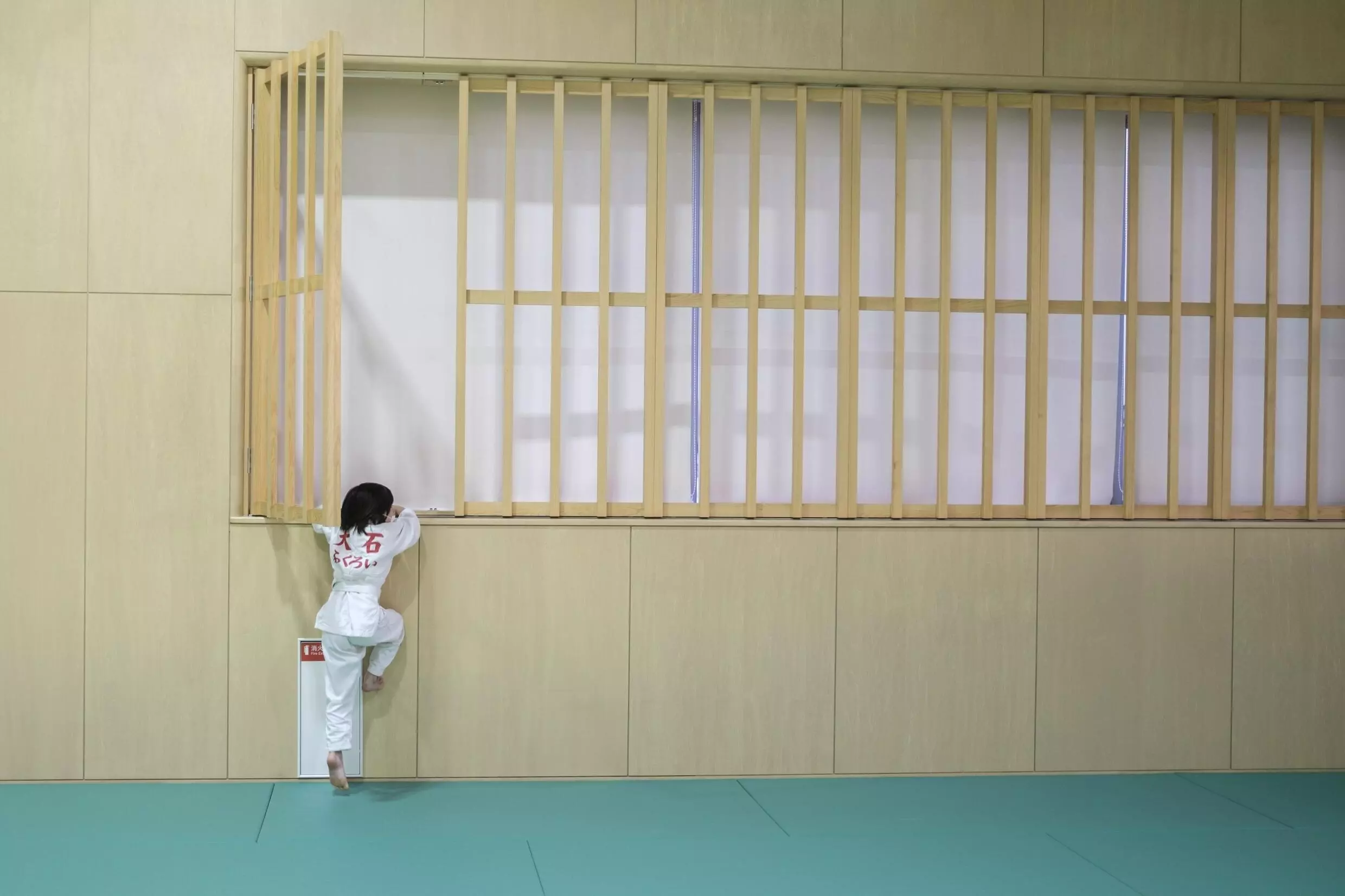 A child climbs up to a windowsill to open curtains before a judo training session in Fukuroi, Shizuoka prefecture. Photo: AFP