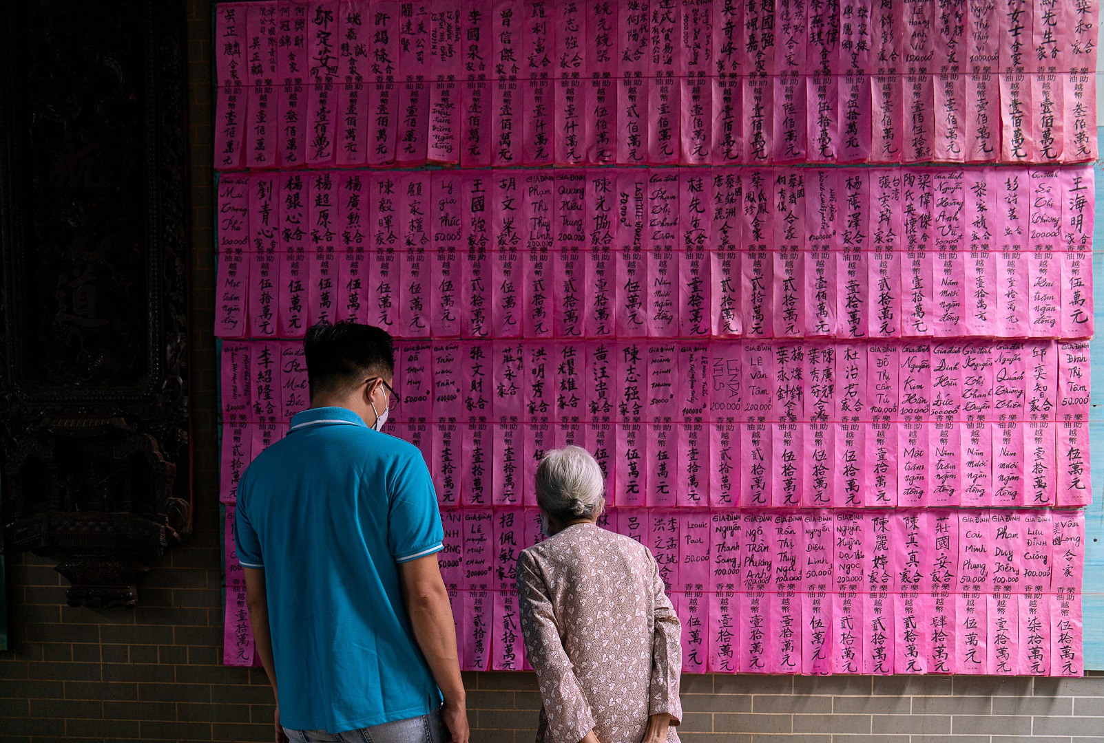 Visitors look at pink pieces of paper, on which names of pilgrims and their contributions to the temple are written, stuck on a wall of the temple. Photo: Nguyen Trung Au / Tuoi Tre News